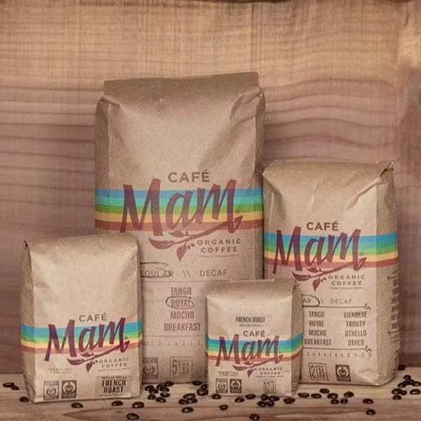 Four bags of "Café Mam Organic Coffee" in various sizes, with coffee beans scattered around.