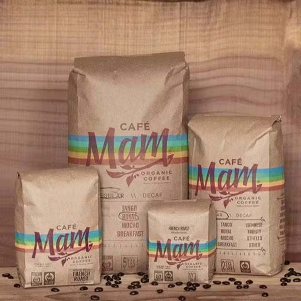 Four bags of "Café Mam Organic Coffee" in various sizes, with coffee beans scattered around.
