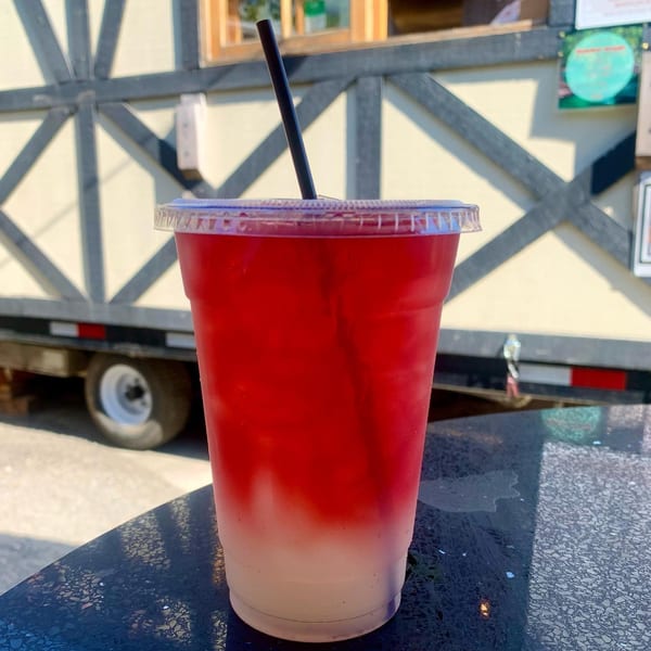 A red and white layered drink with a black straw sits on a dark table outdoors.